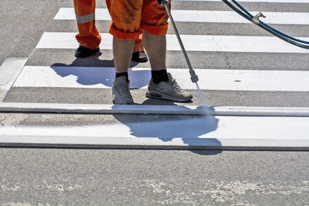 Workers are painting a pedestrian crossing in a city street.の写真素材