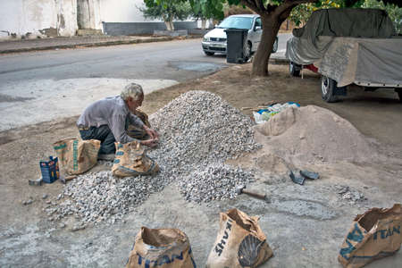 Loutra Edipsou, Greece, May 30, 2016. An elderly gentleman works hard all day with a hammer in the heat to break and crush stones on the street.のeditorial素材