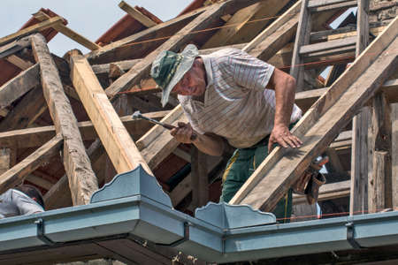 Zrenjanin, Serbia, July 22, 2020. A master works on the roof of a private house to replace the roof tile. He is part of the team that does it. It currently strengthens one supporting beam.のeditorial素材