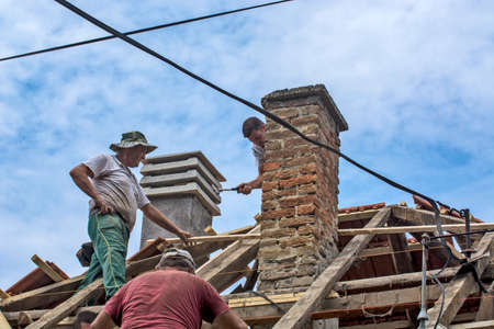 Zrenjanin, Serbia, July 22, 2020. A group of masters is working on the roof of a private house to replace an old tile. They use a nice day and stable weather without rain. They are disturbed by various cables that run over the roof of the house.のeditorial素材