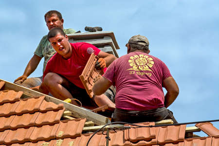 Zrenjanin, Serbia, July 23, 2020. A group of masters is working on the roof of a private house to replace an old tile. They use a nice day and stable weather without rain. They are disturbed by various cables that run over the roof of the house.のeditorial素材
