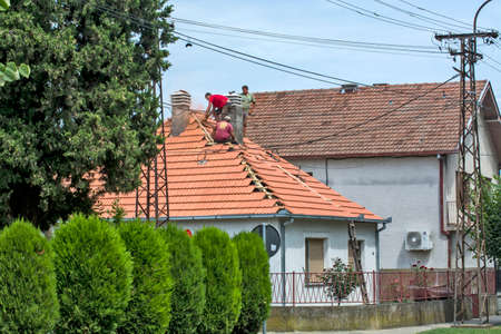 Zrenjanin, Serbia, July 23, 2020. A group of masters is working on the roof of a private house to replace an old tile. They use a nice day and stable weather without rain. They are disturbed by various cables that run over the roof of the house.のeditorial素材