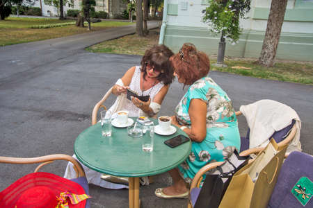 Zrenjanin, Serbia, September 06, 2019. Two friends are sitting in a cafe and talking casually about photos on their phones.のeditorial素材