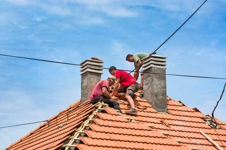 Zrenjanin, Serbia, July 23, 2020. A group of masters is working on the roof of a private house to replace an old tile. They use a nice day and stable weather without rain. They are disturbed by various cables that run over the roof of the house.のeditorial素材