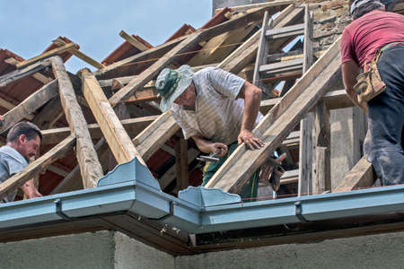 Zrenjanin, Serbia, July 22, 2020. A group of masters is working on the roof of a private house to replace an old tile. They use a nice day and stable weather without rain. They are disturbed by various cables that run over the roof of the house.のeditorial素材