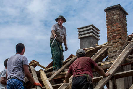 Zrenjanin, Serbia, July 22, 2020. A group of masters is working on the roof of a private house to replace an old tile. They use a nice day and stable weather without rain. They are disturbed by various cables that run over the roof of the house.のeditorial素材