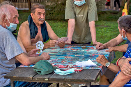 Zrenjanin, Serbia, July 29, 2020. Older gentlemen and pensioners play cards every day in the shade of a large tree. There are always curious observers.のeditorial素材