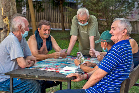 Zrenjanin, Serbia, July 29, 2020. Older gentlemen and pensioners play cards every day in the shade of a large tree. There are always curious observers.のeditorial素材