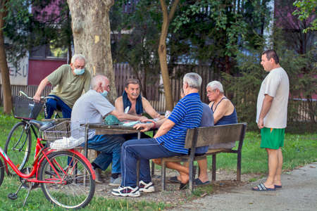 Zrenjanin, Serbia, July 29, 2020. Older gentlemen and pensioners play cards every day in the shade of a large tree. There are always curious observers.のeditorial素材