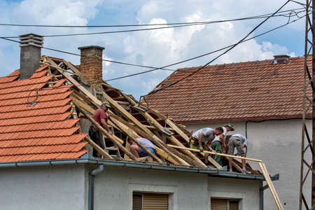 Zrenjanin, Serbia, July 22, 2020. A group of masters is working on the roof of a private house to replace an old tile. They use a nice day and stable weather without rain. They are disturbed by various cables that run over the roof of the house.のeditorial素材