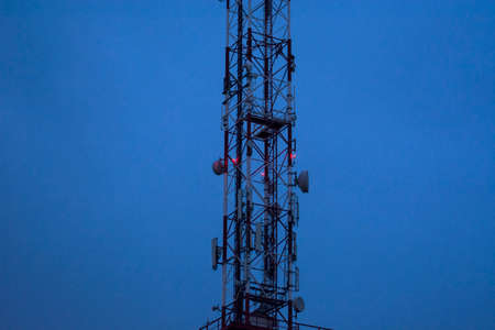 Part of a telecommunication pole at dusk. The night warning lights on the pole came on.