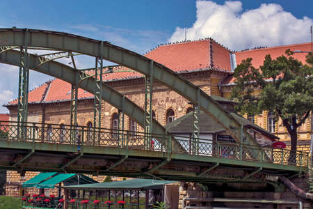 Zrenjanin, Serbia, July 04, 2020. Old bridge, restaurant below and a large old building. There is a large number of pigeons on the roof of the building.のeditorial素材