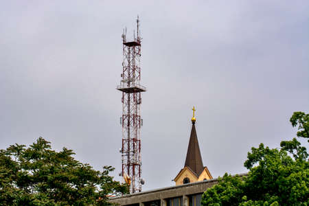 A telecommunication pole and a church tower that can be seen in the distance behind the concrete hall. Symbols of modern technology and religion.の写真素材