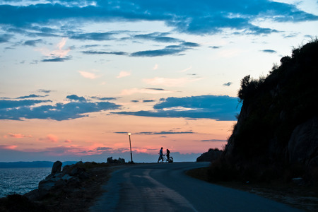 Young couple with tandem bicycle at greek sea coast after sunset, Sithonia, Greeceの写真素材