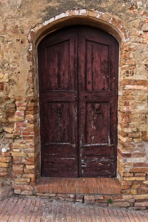 Architectural details of a weathered doors on an old brick house in a narrow winding streets at San Gimignano, Tuscany, Italyの写真素材