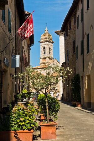 Narrow cobblestone street leading to San Quirico church at sunny morning in San Quirico d'Orcia , Siena province, Tuscany, Italyの写真素材