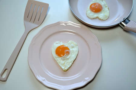 Heart shaped eggs on a pink plate with a pink pan and spatula.
