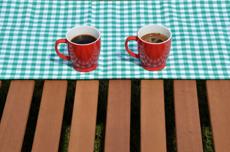 Coffee cups set outdoor on a green and white tablecloth and wooden surfaceの写真素材