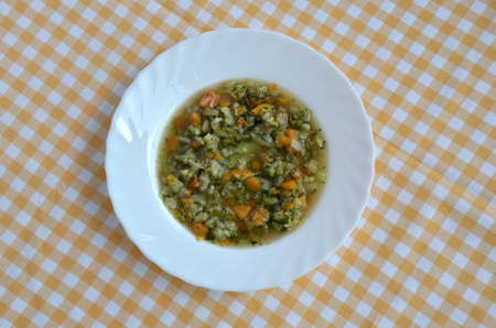 Spring vegetable soup in a white plate on yellow white tablecloth.の写真素材