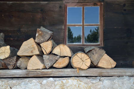 Logs on a porch of an old village house with a window  behind.の写真素材