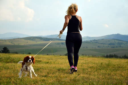 Lady jogging with her cavalier king charles spaniel in the mountainsの写真素材