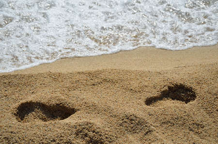 Footprints in opposite direction on beach with sea foam in backgroundの写真素材