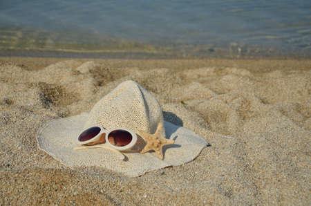 Straw hat, glasses and sea star set on a beach with sea in backgroundの写真素材