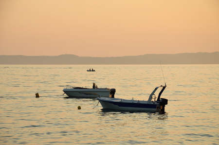 Two boats on sea with a third one and mountains in background in sunset timeの写真素材