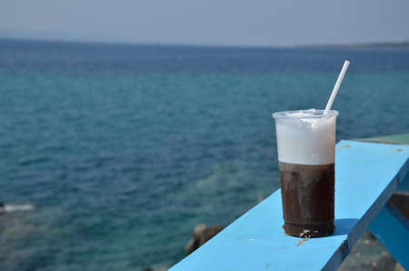 Glass with just made cappuccino on blue beach bar table with sea in backgroundの写真素材
