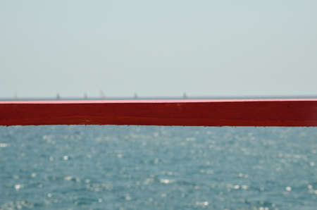 Red plank with turquoise sea and silhouettes of sailing boats in backgroundの写真素材