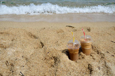 Cold coffee frappes set on beach with a wave in backgroundの写真素材