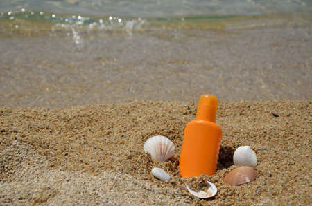 Sun lotion with sea shells on a beach with sea in background