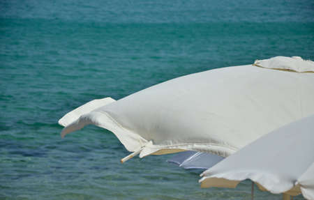 White beach parasol with blurred turquoise sea on windy dayの写真素材