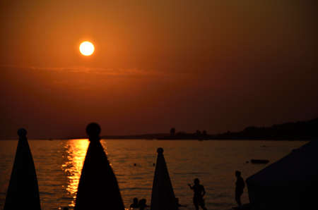 Closed beach parasols and visitors in sunsetの写真素材