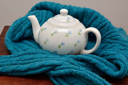 Tea pot wrapped with turquoise woolen jumper on brown wooden surfaceの写真素材
