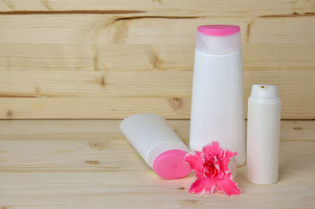 White-pink bottles of lady's cosmetics with pink flower on wooden surface