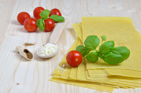 Lasagna sheets with fresh basil leaves, cherry tomatoes, grated hard cheese and nutmeg, laid on kitchen deskの写真素材