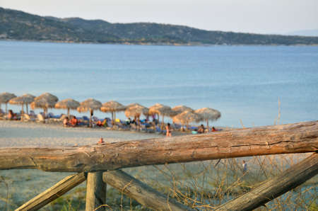 Greek blue sea and parasols on the beach behind wooden fenceの写真素材