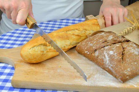 Someone is cutting white baguette and dark bread with knife