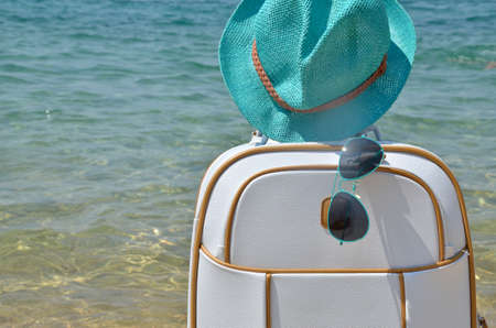 Suitcase, hat and sunglasses on beach with sea in backgroundの写真素材