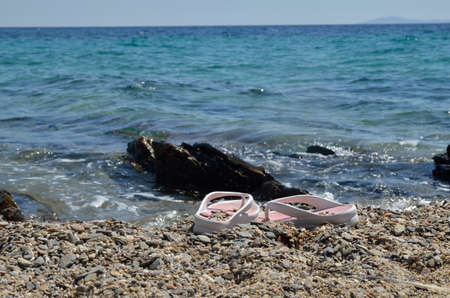 White-pink flip-flops left on beach sand with sea shallow in backgroundの写真素材