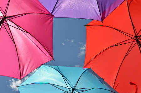 Parts of pink, violet, red and blue umbrella with a part of blue sky for copy textの写真素材