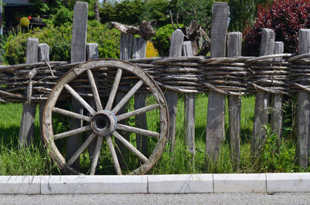 Rustic wheel of a traditional cart leaning on a wooden fenceの写真素材