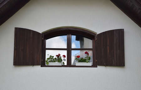 Brown wooden window on white wall of a mountain house with reflection of white cloud on a blue skyの写真素材