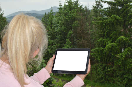 Blonde woman with ponytail looking at landscape and her tablet white screen suitable for copy text...