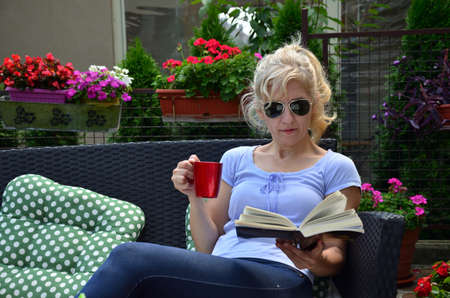 Closeup of a woman with a cup of coffee or tea and a book in a gardenの写真素材
