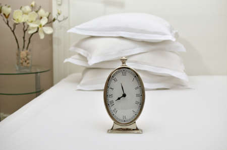 Alarm clock showing five to eight on a bed with pillows in backgroundの写真素材