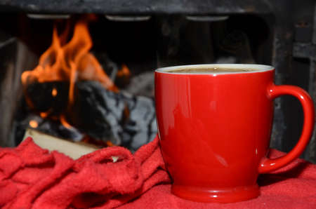 Red cup on a red soft blanket with fire form a fireplace in backgroundの写真素材