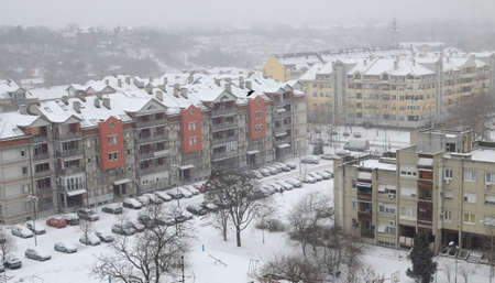 Block of residential buildings with church tower covered with snow during snowfallの写真素材