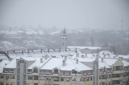 Block of residential buildings with church tower covered with fresh snow on foggy dayの写真素材